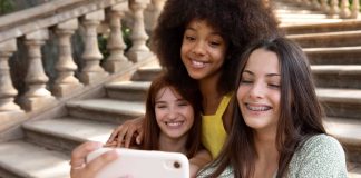 Três meninas - uma negra, uma ruiva e outra de cabelo preto - tiram selfie com celular