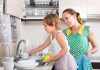 Mãe olha filha lavando pratos da casa
