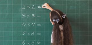 garota de costas escrevendo multiplicações no quadro negro