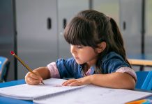 Menina sentada escreve no caderno sobre carteira escolar