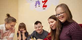 Crianças com síndrome de down sorrindo, sentadas a mesa e estudando com seus amigos