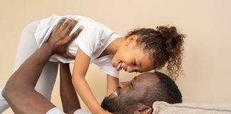 Pai negro deitado na cama segura filha nos braços