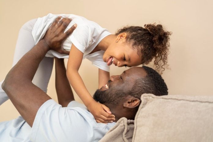 Pai negro deitado na cama segura filha nos braços