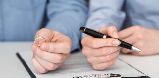Mão masculina segura aliança e mão feminina segura caneta com documento do divórcio na mesa, práticas colaborativas são nova tendência