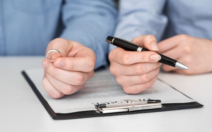 Mão masculina segura aliança e mão feminina segura caneta com documento do divórcio na mesa, práticas colaborativas são nova tendência