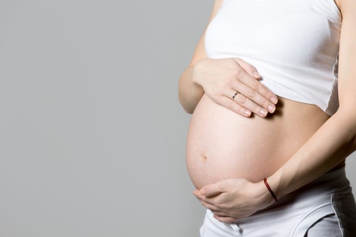 Mulher grávida em pé, com as mãos na barriga