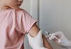 Criança de camiseta rosa recebe vacina no braço esquerdo