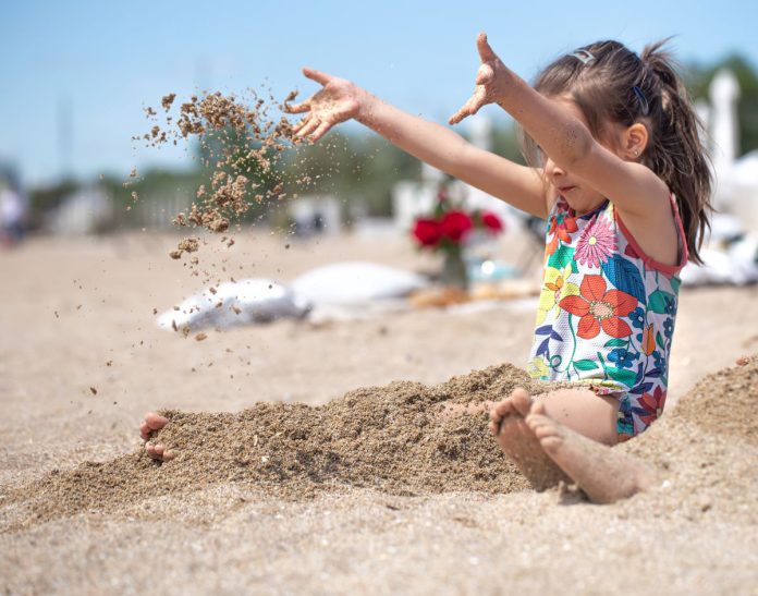 Criança na praia de maiô brincando com areia