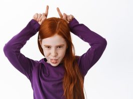 Menina com cara de má faz sinal de diabinha com dedos indicadores levantados sobre a cabeça