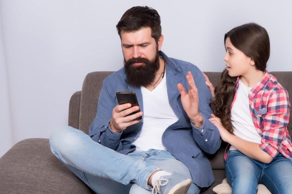 The father looks at the cell phone and ignores the girl trying to talk to him