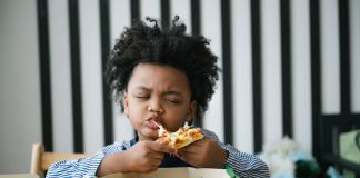 Menino come pedaço de pizza com a mão