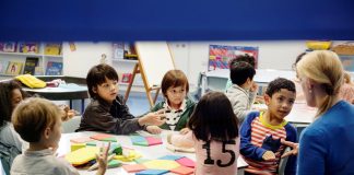 Crianças fazem atividade escolar sentadas todas juntas em mesa na sala de aula