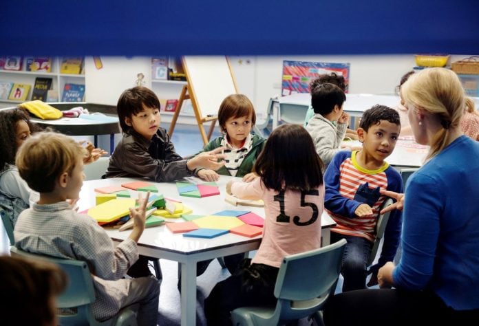 Crianças fazem atividade escolar sentadas todas juntas em mesa na sala de aula