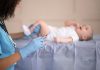 Bebê deitado, enquanto enfermeira aplica uma vacina