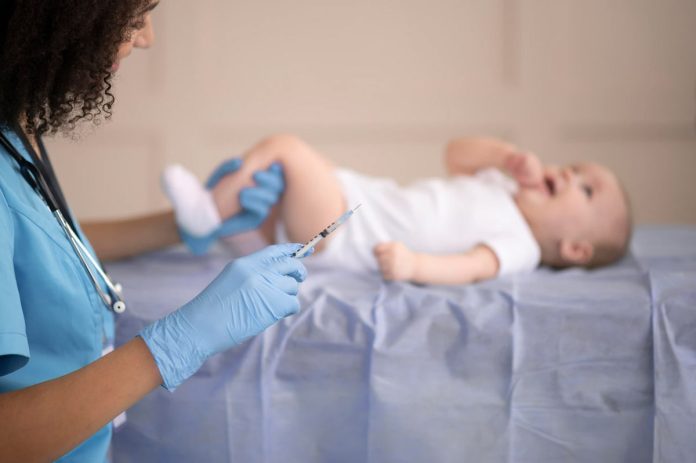 Bebê deitado, enquanto enfermeira aplica uma vacina