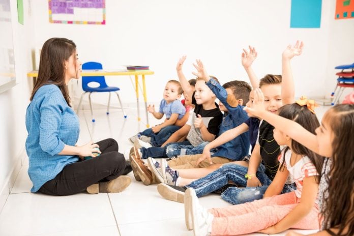 Crianças sentadas no chão conversam com professora
