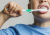 Menino de camiseta azul escova os dentesexcesso de creme dental, que pode provocar fluorose dentária nas crianças; imagem mostra rosto de menino escovando os dentes