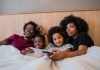 Pais e dois filhos deitados na cama, assistindo filme juntos
