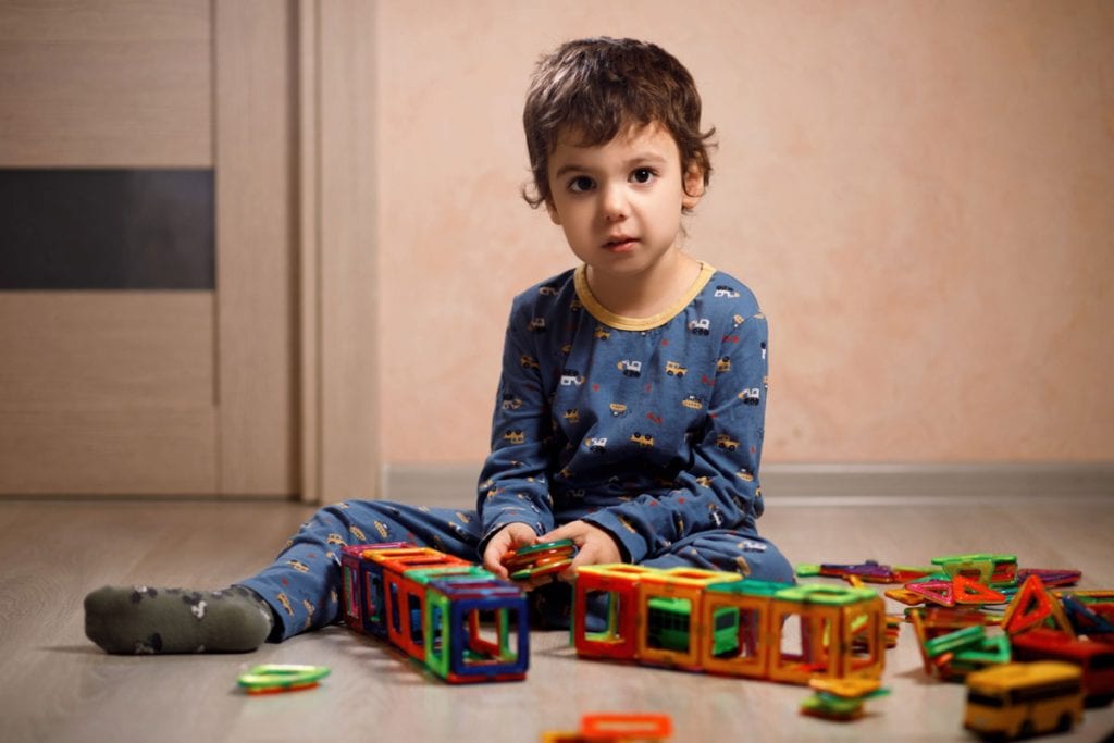 Criança sentada no chão, olhando para frente, com brinquedos espalhados no chão