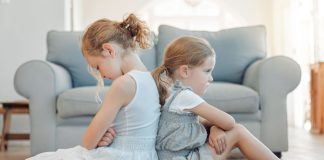 Briga entre irmãos: meninas estão sentadas no chão com as costas apoiadas uma na outra com cara de bravas