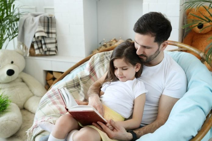 Pai e filha leem livro juntos sentados em poltrona