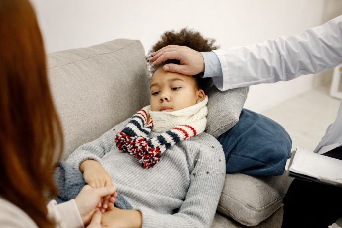 Menina de cabelos crespos está deitada no sofá e médico está com a mão na sua testa
