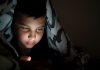 A geração do quarto vive plugada à internet, como esse menino, que está coberto por edredon, e olha tela de celular no escuro