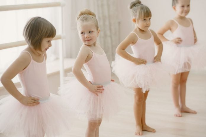 Quatro meninas fazem aula de balé com collant e saia rosa