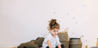 Menina brinca sobre tapete com almofadas, manta e livro