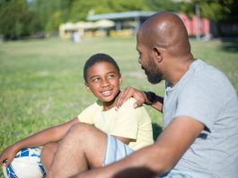 Pai e filho conversam sentados em campo de futebol