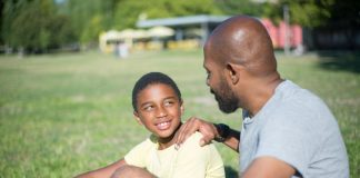 Pai e filho conversam sentados em campo de futebol