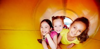 Crianças brincam dentro de tobogã amarelo