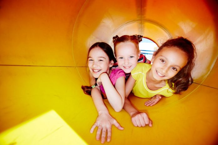 Crianças brincam dentro de tobogã amarelo