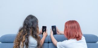 Dois adolescentes no sofá seguram na mão um celular e na tela se vê imagem do Tik tok