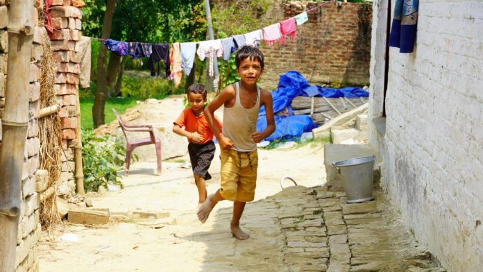 Dois meninos correm em área externa de vila de casas simples