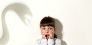 Criança com expressão de medo na parede que tem sombra assustadora