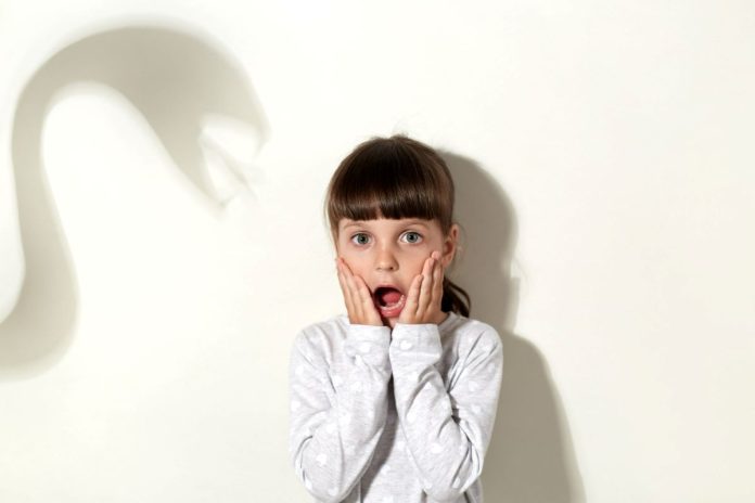Criança com expressão de medo na parede que tem sombra assustadora