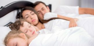 Dias crianças dormem na cama de casal junto com a mãe e o pai
