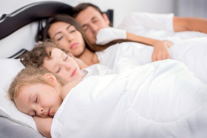Dias crianças dormem na cama de casal junto com a mãe e o pai
