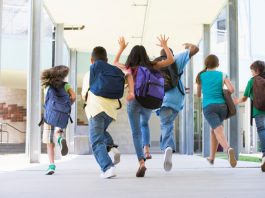 Alunos com mochila nas costas correm no corredor da escola