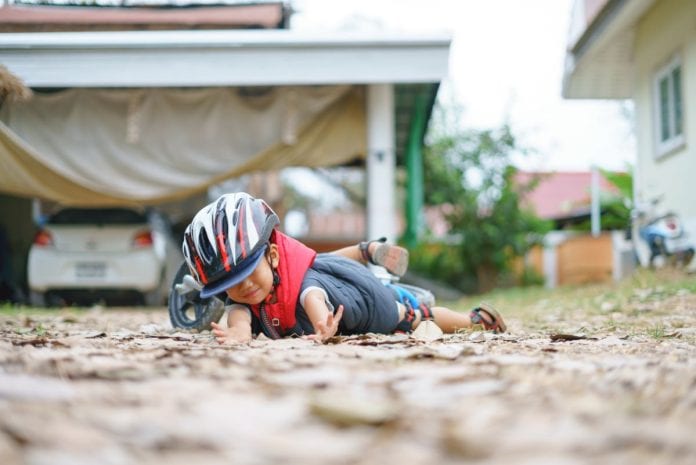 Criança de capacete levou uma queda e está deitada no chão