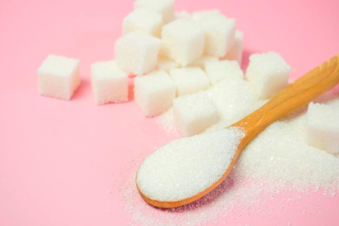 Açúcar granulado e cubos de açúcar em um fundo rosa
