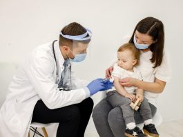 Homem aplica vacina em bebêno colo da mãe
