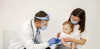 Homem aplica vacina em bebêno colo da mãe