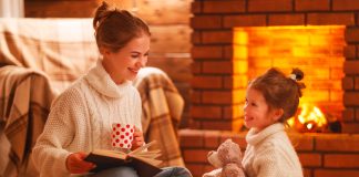 Mãe e filha leem livro próximas à lareira da casa