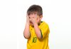 Menino com camiseta da seleção brasileira tampa olhos com as mãos