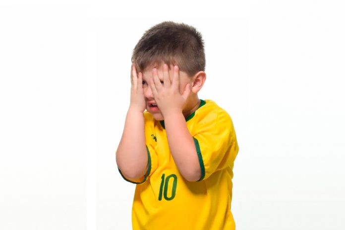 Menino com camiseta da seleção brasileira tampa olhos com as mãos