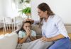 Tosse, vômitos e dor abdominal: saiba como lidar com as queixas mais comuns na pediatria; criança doente assoando o nariz e mãe a confortando