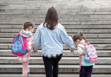 Mãe sobe escadaria de mãos dadas com duas filhas com mochilas nas costas