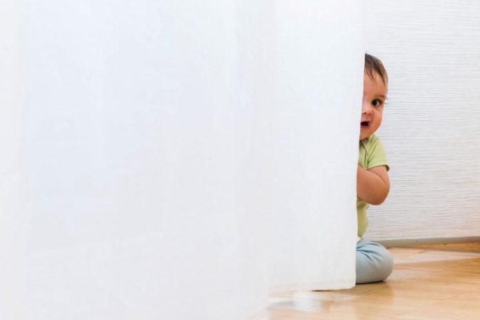 Criança pequena no chão se esconde por trás da parede